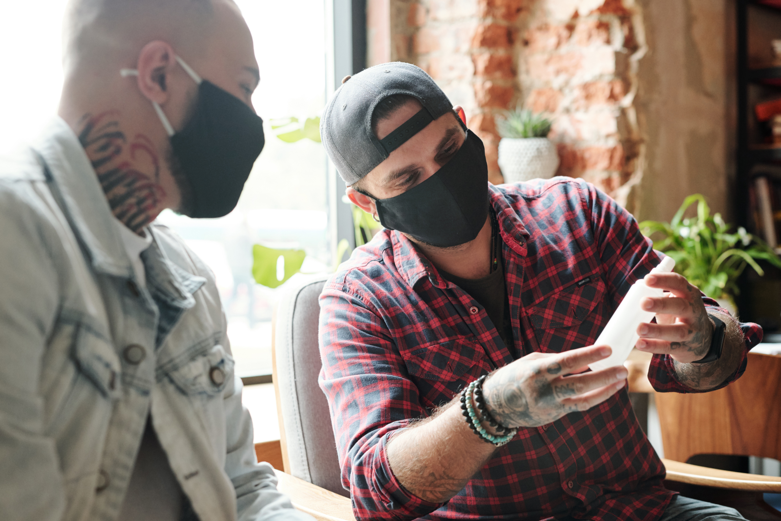 A nurse practitioner supports a young man as part of a community response team. Both are wearing black face masks and are sitting in a community cafe.